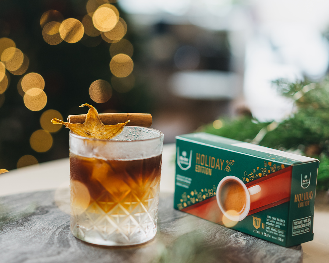 Ginger coffee tonic servido en vaso de vidrio y adornado con una astilla de canela y carambola deshidratada y una caja de cápsulas de Britt Espresso Holiday Edition 2025