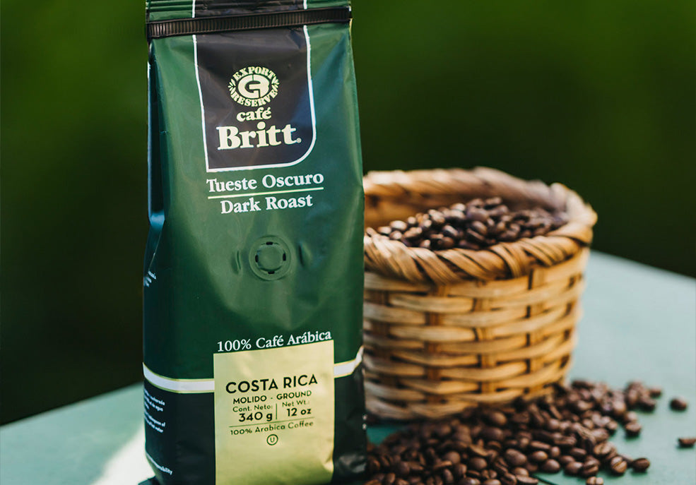 Bolsa de café molido Café Britt Tueste Oscuro junto a una canasta con granos de café.