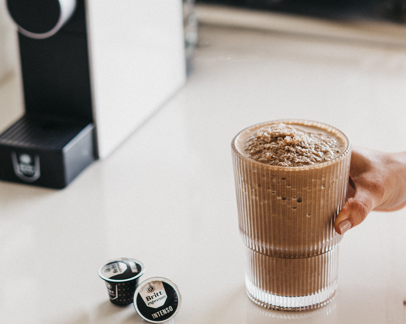 Vaso de Protein Mocha preparado con café espresso y cápsulas Café Britt junto a una máquina de café.