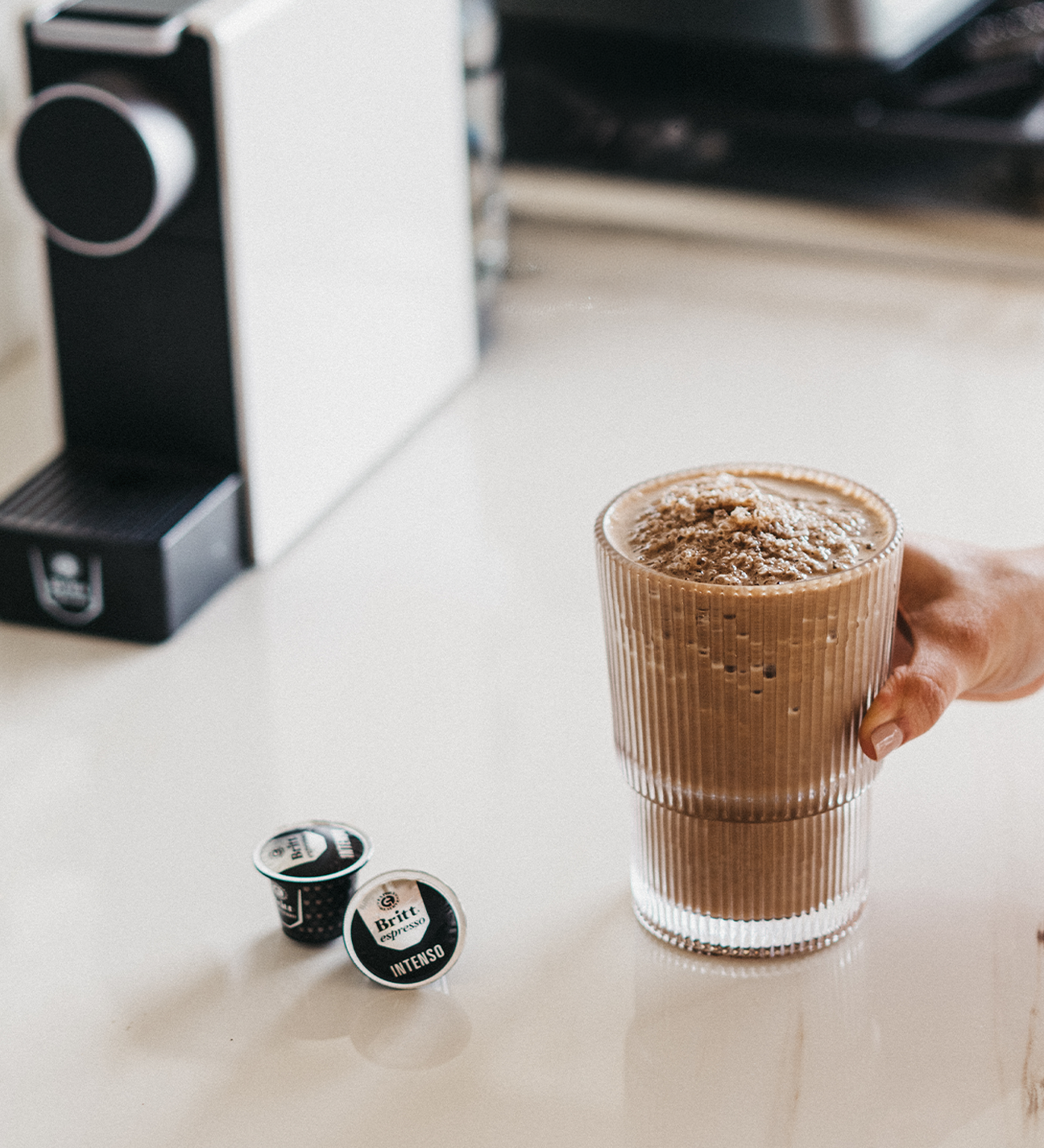 Vaso de Protein Mocha preparado con café espresso y cápsulas Café Britt junto a una máquina de café.