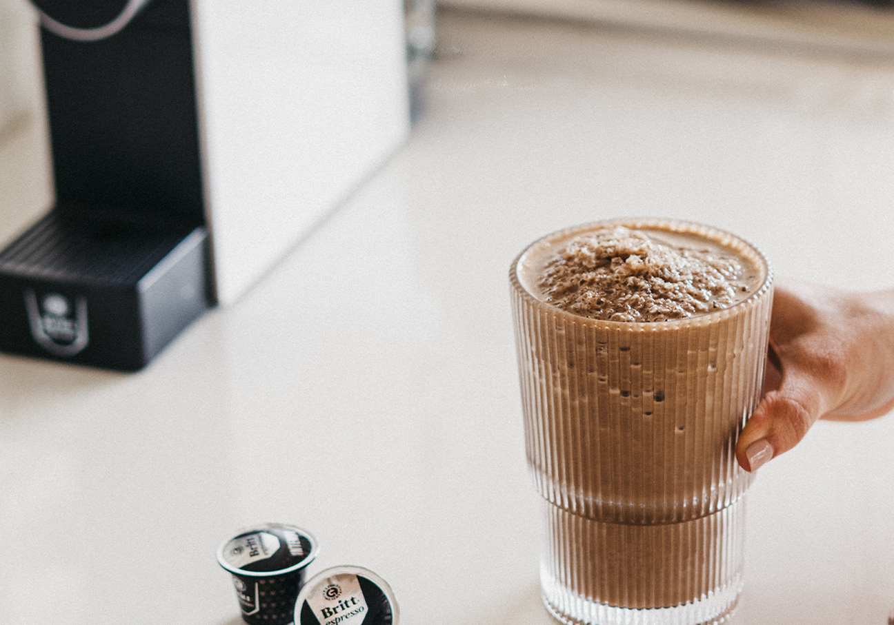 Vaso de Protein Mocha preparado con café espresso y cápsulas Café Britt junto a una máquina de café.