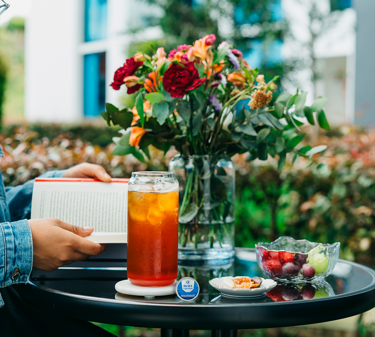 Mocktail de San Valentín servido con hielo, acompañado de frutas frescas y un libro sobre una mesa al aire libre.