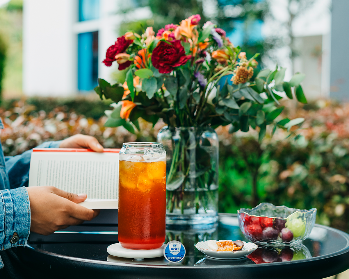 Mocktail de San Valentín servido con hielo, acompañado de frutas frescas y un libro sobre una mesa al aire libre.