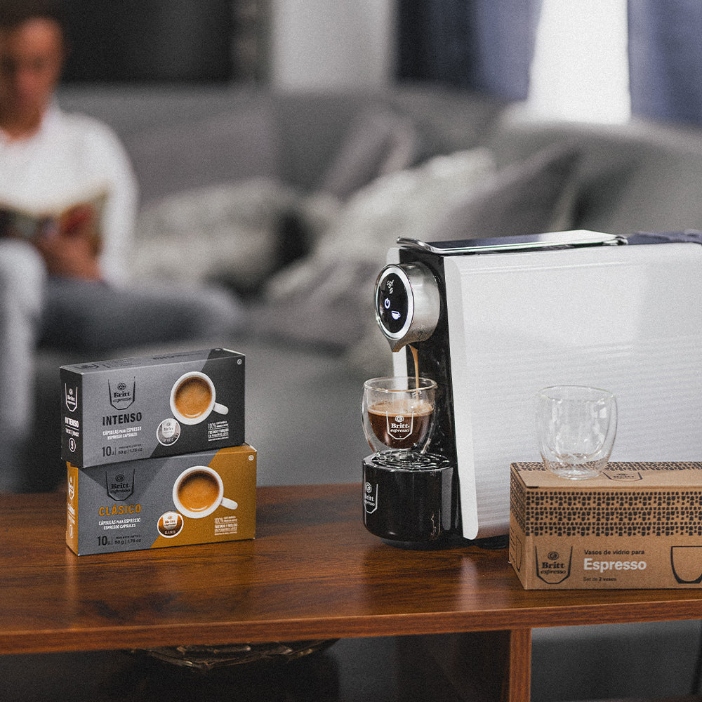 Mesa con máquina de cáspsulas britt espresso nova, 2 cajas de cápsulas Britt Espresso y 2 set de vasos de vidrio para espresso.